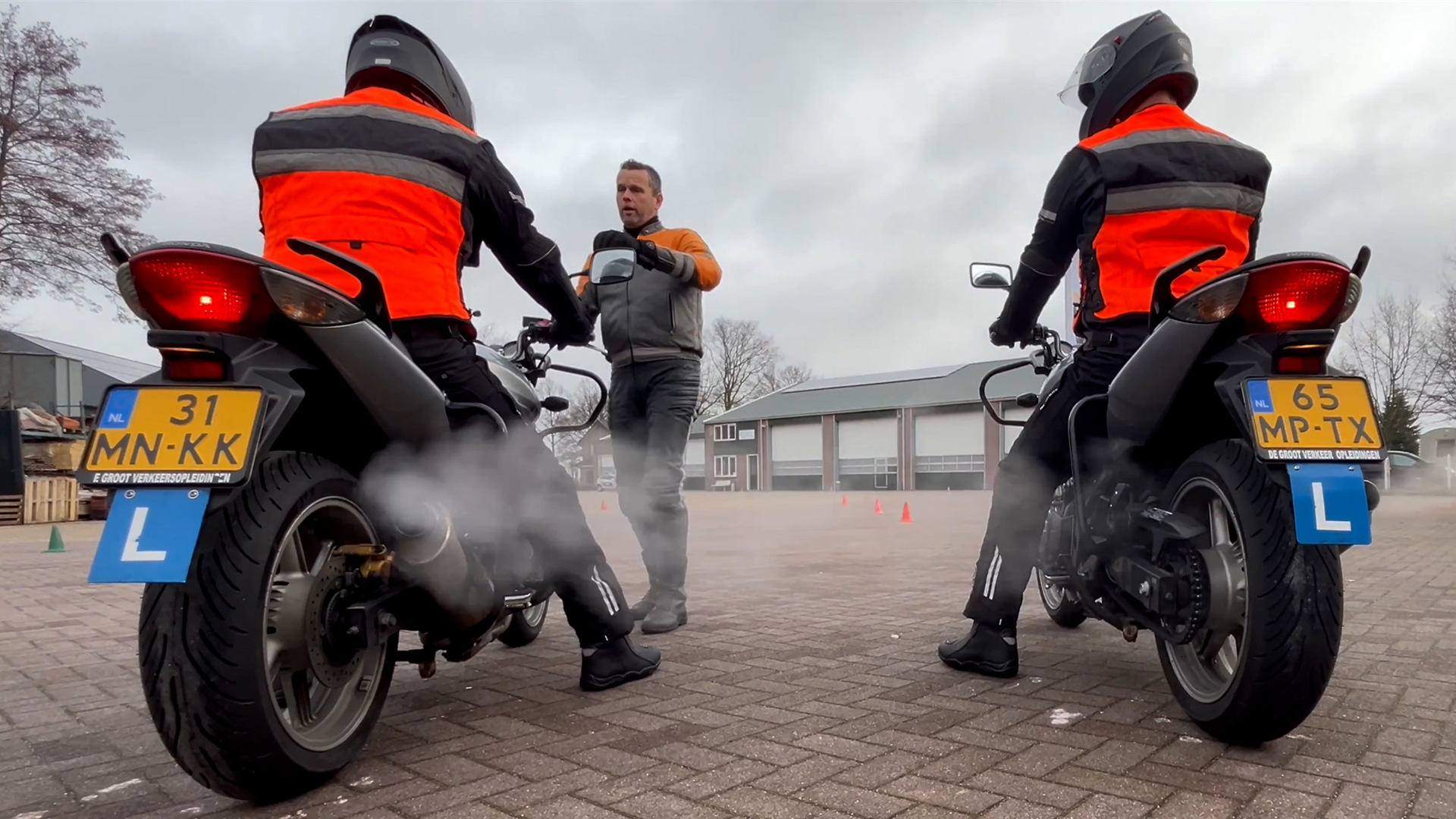 Driving instructor gives motorcycle riding lessons to two students on the practice grounds of a motorcycle driving school