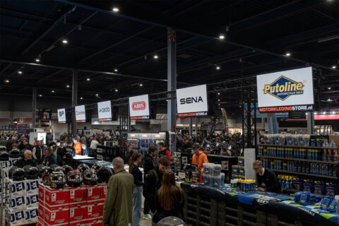 Drukke Motorkledingstore-stand op MOTORbeurs Utrecht met helmen, accessoires en borden van merken als Putoline, SENA en ABUS
